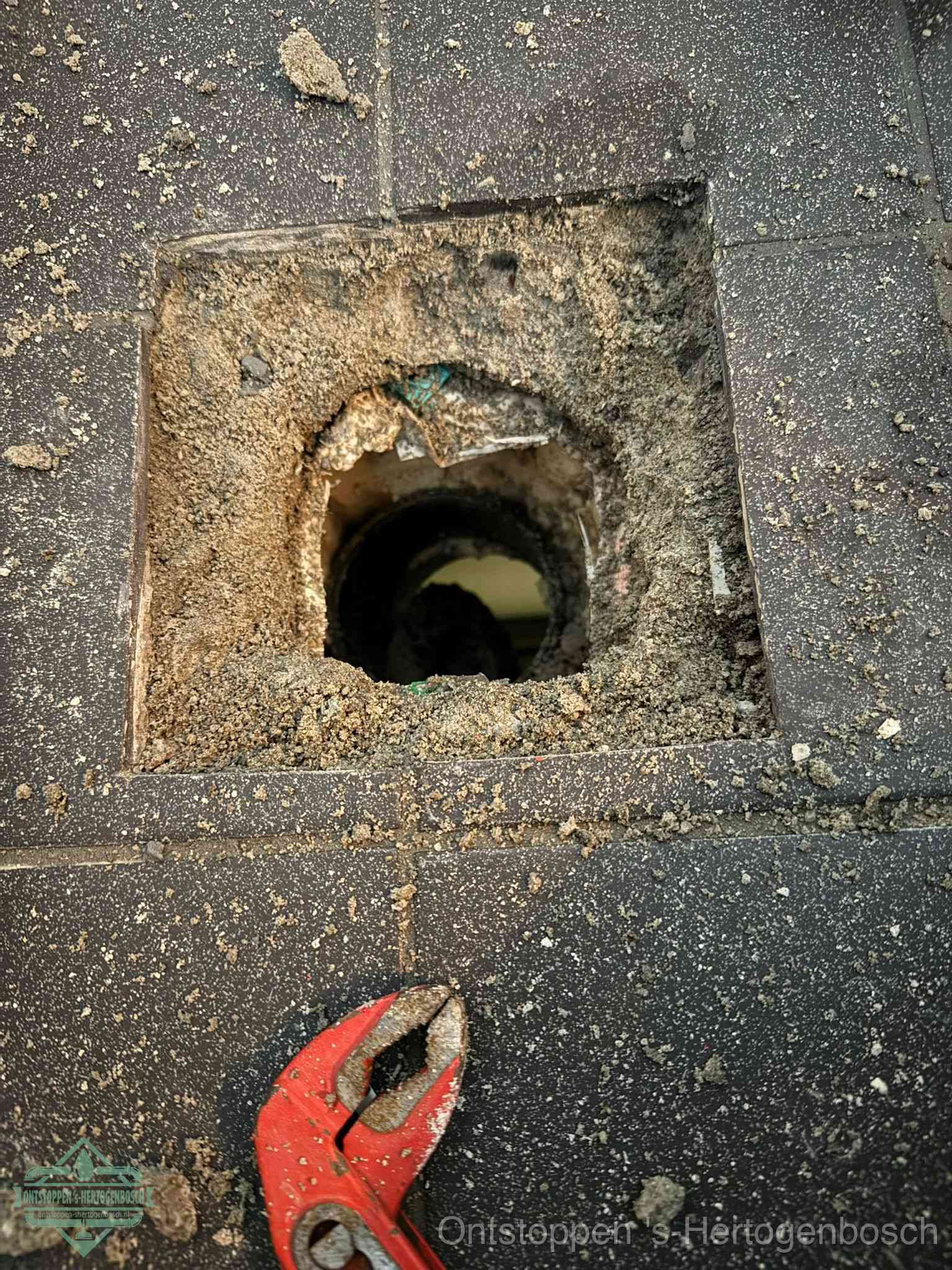 Een geopend rioolputje in een betontegelvloer met losgemaakt rooster en een zichtbare ronde afvoerbuis, het achterhalen waar de afvoerverstopping zit in s-Hertogenbosch