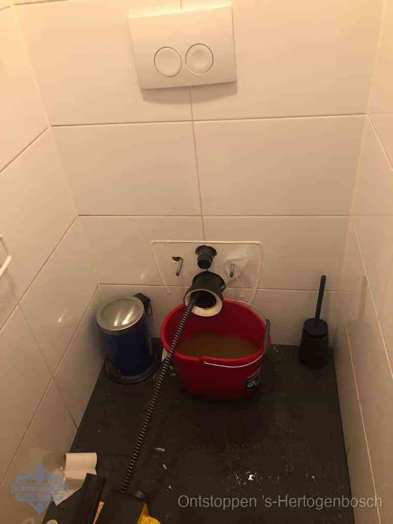Een ontstopte wand-wc met verwijderde toiletpot waar een ontstoppingsveer in de wanduitgang verdwijnt, het achterhalen waar de verstopping zit in s-Hertogenbosch
