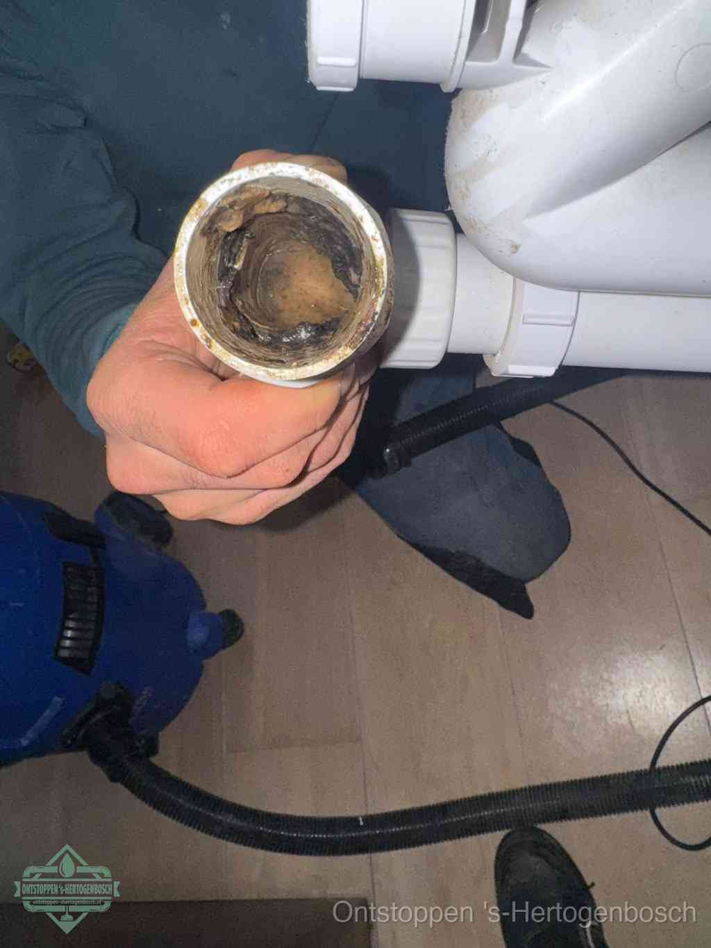 Een hand houdt een losgekoppeld PVC-afvoerbuisstuk vast dat van binnen volledig is dichtgeslibd met vet, vuil en aanslag, de meest voorkomende oorzaak van een verstopte afvoer in s-Hertogenbosch