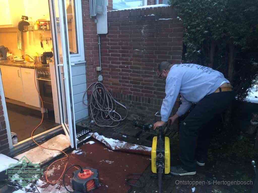 Een monteur werkt buiten bij een open riool-/grondput met een elektrische ontstoppingsmachine om een verborgen afvoerprobleem op te sporen in s-Hertogenbosch