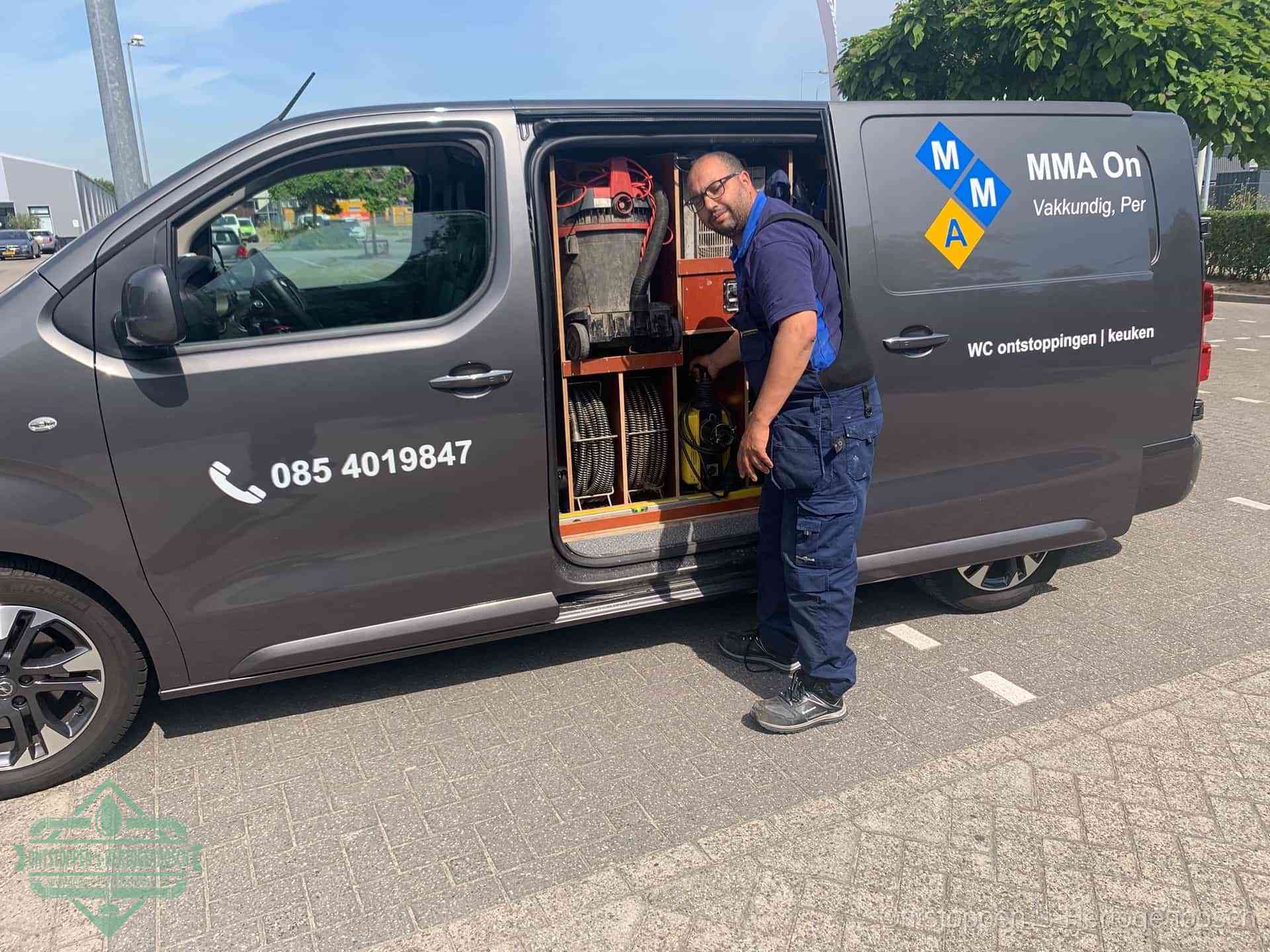 Een monteur bij de open schuifdeur van zijn bedrijfsbus op een parkeerplaats, klaar om de oorzaak van terugkerende afvoerverstoppingen aan te pakken in s-Hertogenbosch