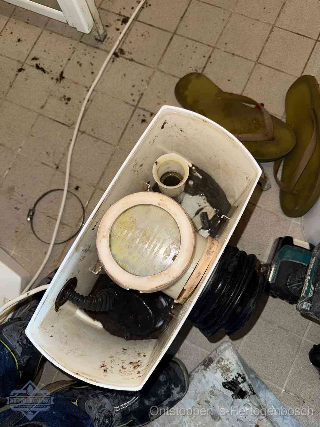 Een gedemonteerde toiletpot op de vloer met ontstoppingsveer en gereedschap ernaast, het verwijderen van een vastzittend voorwerp uit de wc in s-Hertogenbosch